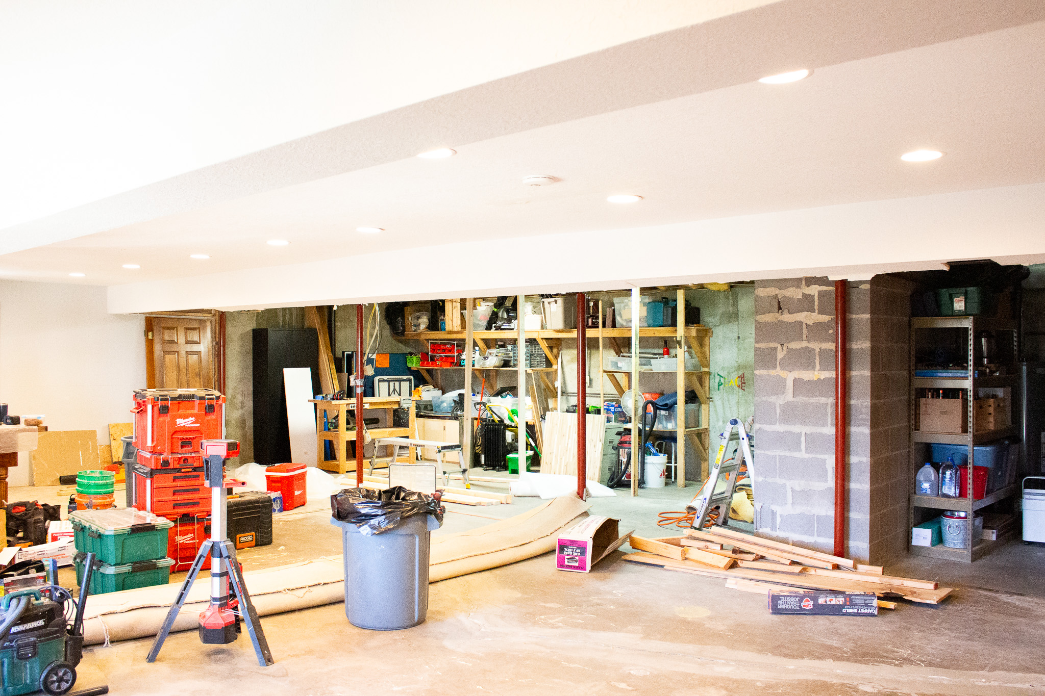 Basement mid-renovation with exposed block wall, steel support posts, and framing lumber staged for finish work.