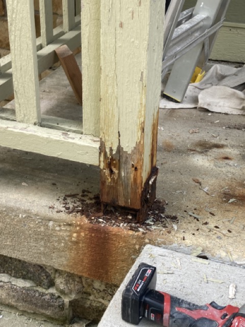 Close-up of a porch railing post with rotted, peeling wood at its base.