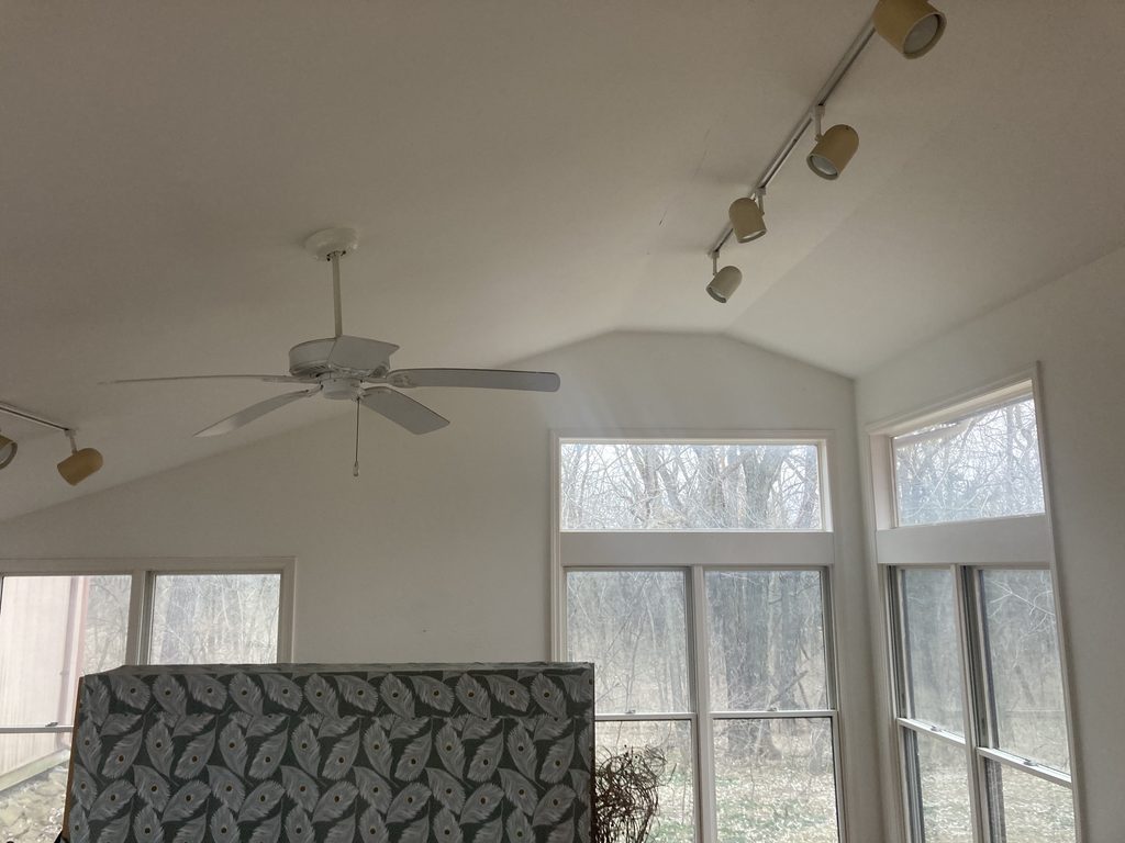 Vaulted ceiling with track lighting and ceiling fan in the sunroom before drywall repairs.