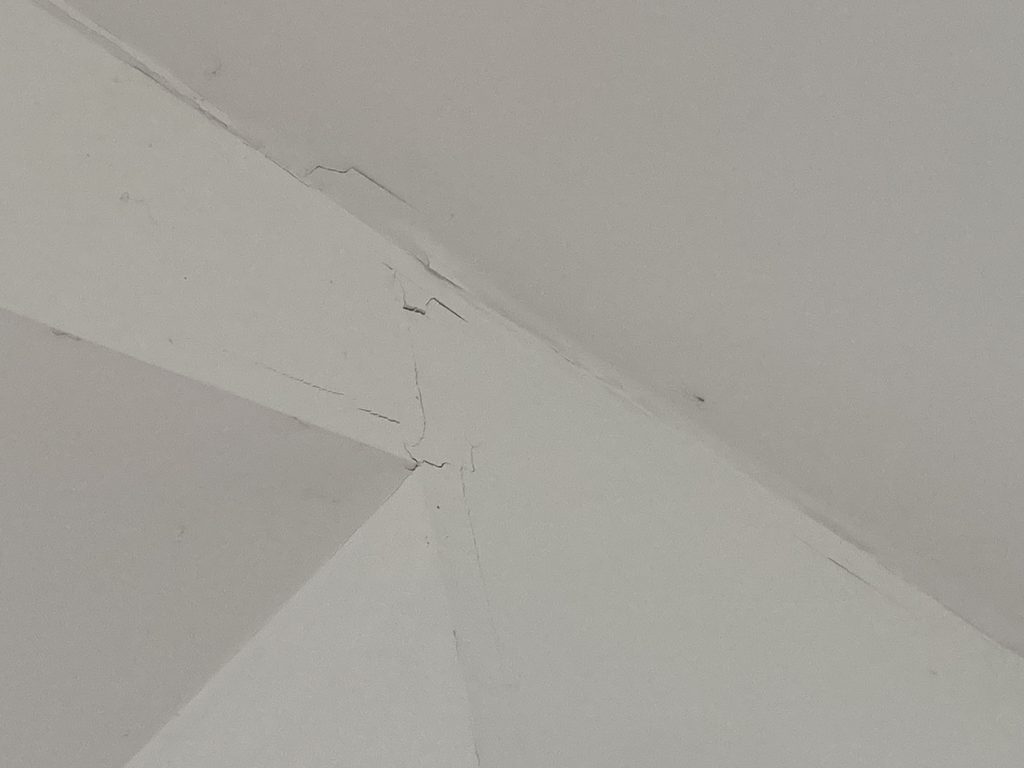 Close-up of a hairline crack running along a ceiling corner before drywall repair.