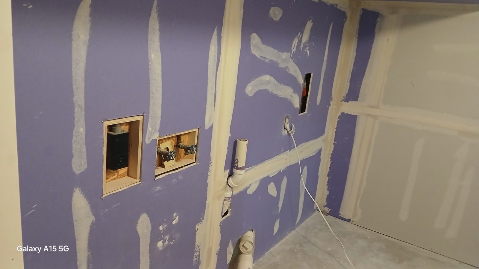 Purple fire-rated drywall hung in laundry room with openings for washer hookup plumbing.