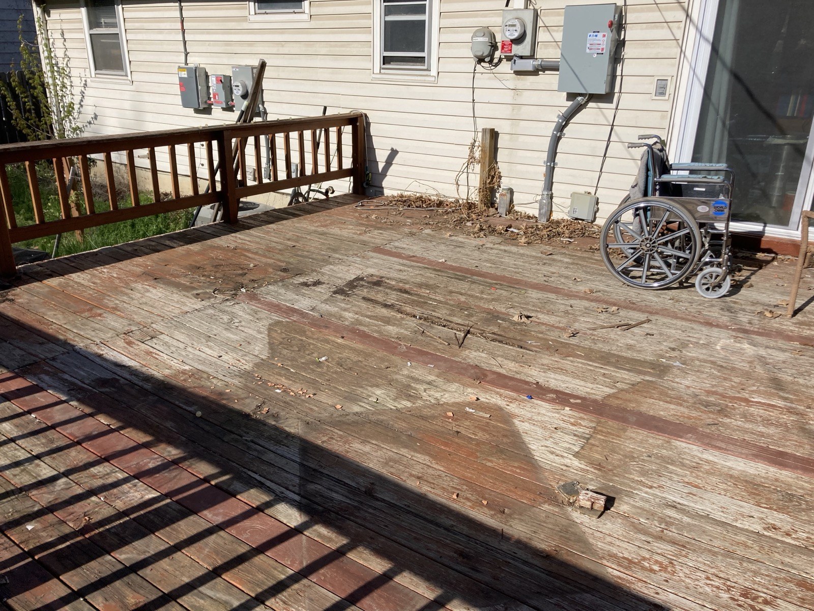 Existing deck surface cleared of furniture, showing worn boards next to the house with a wheelchair parked on the deck