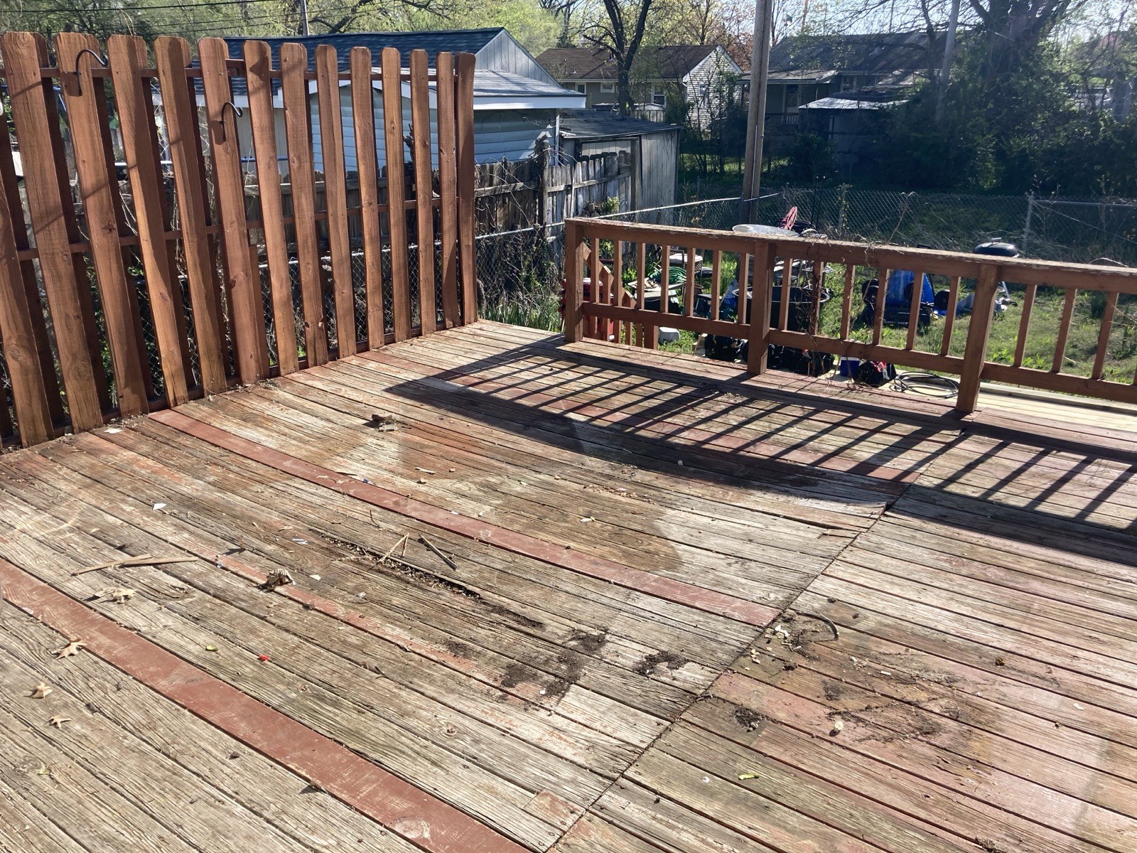 Corner of the existing deck showing weathered decking and railing with the neighborhood visible beyond the fence