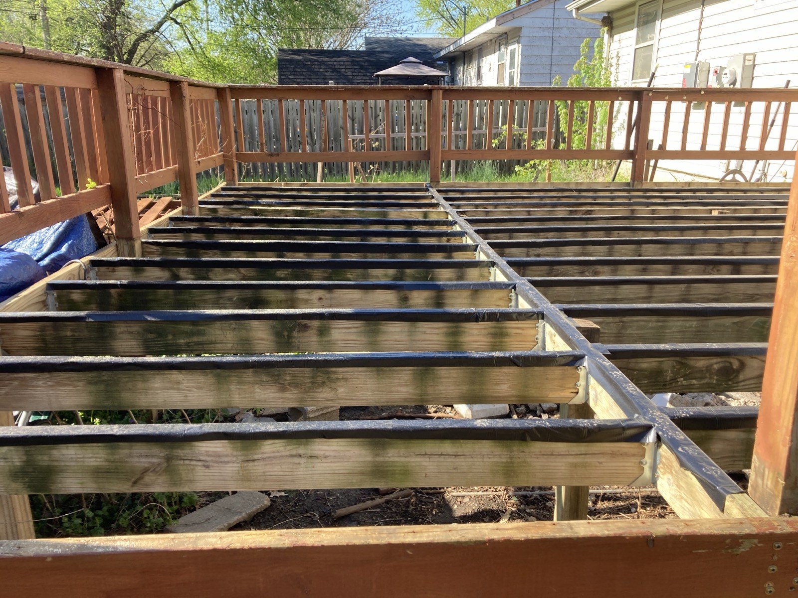 Wider view of the exposed joist framing after the old decking was removed, with the existing railing still in place above