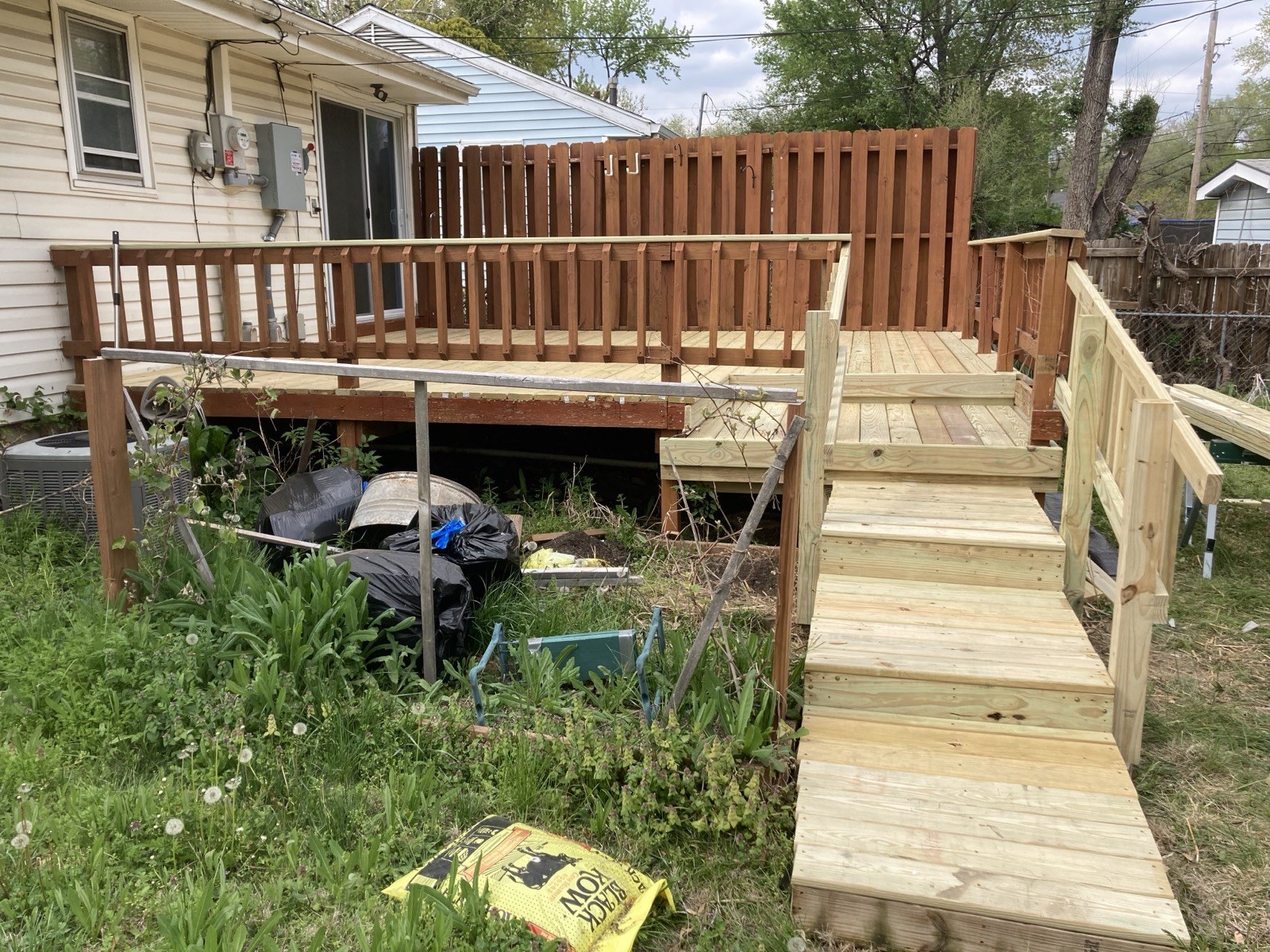 Finished deck and ramp viewed from the house, with new decking, railings, and stairs down to the yard