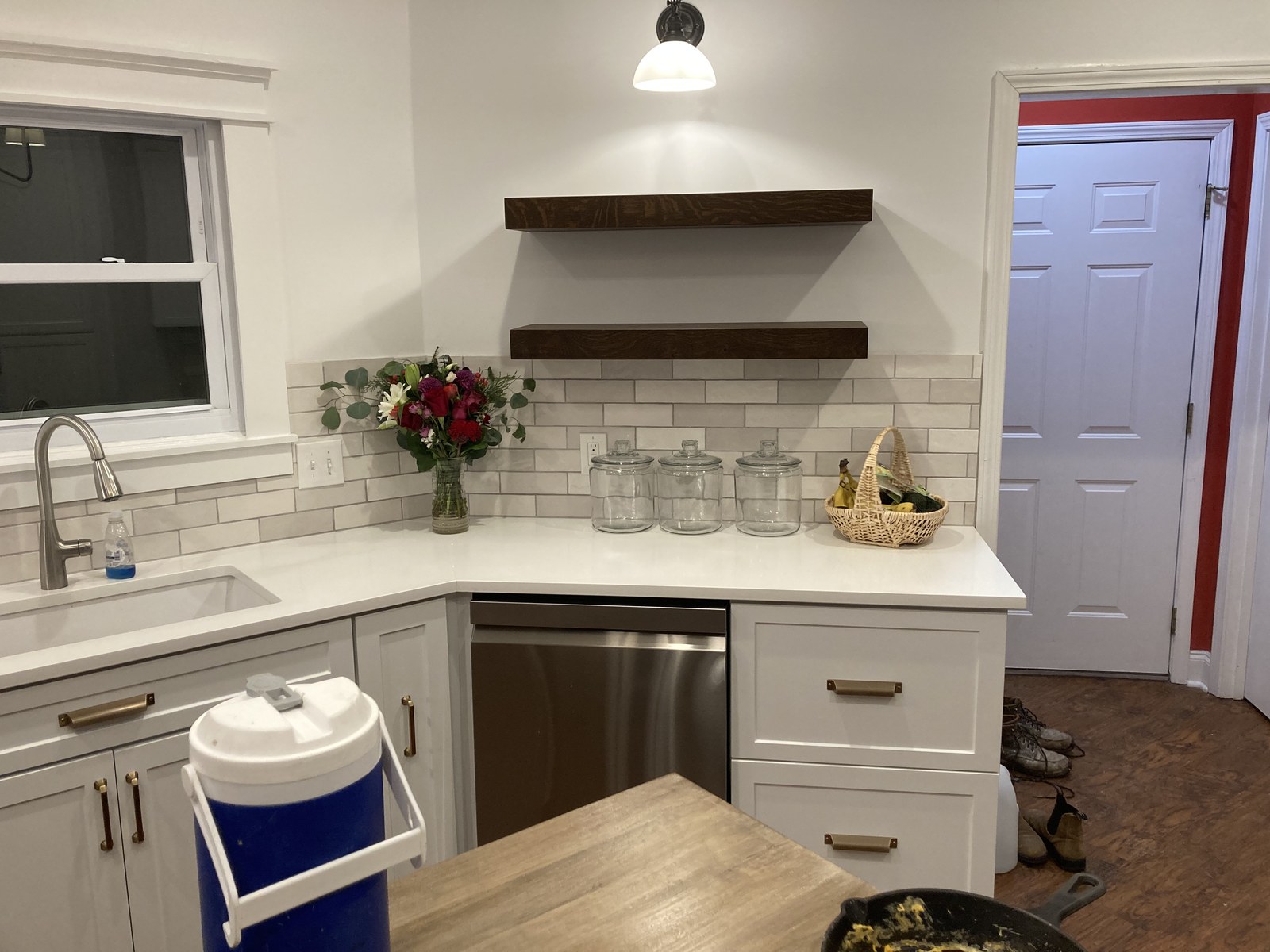 Corner kitchen sink under a window with dark wood floating shelves above a subway tile backsplash