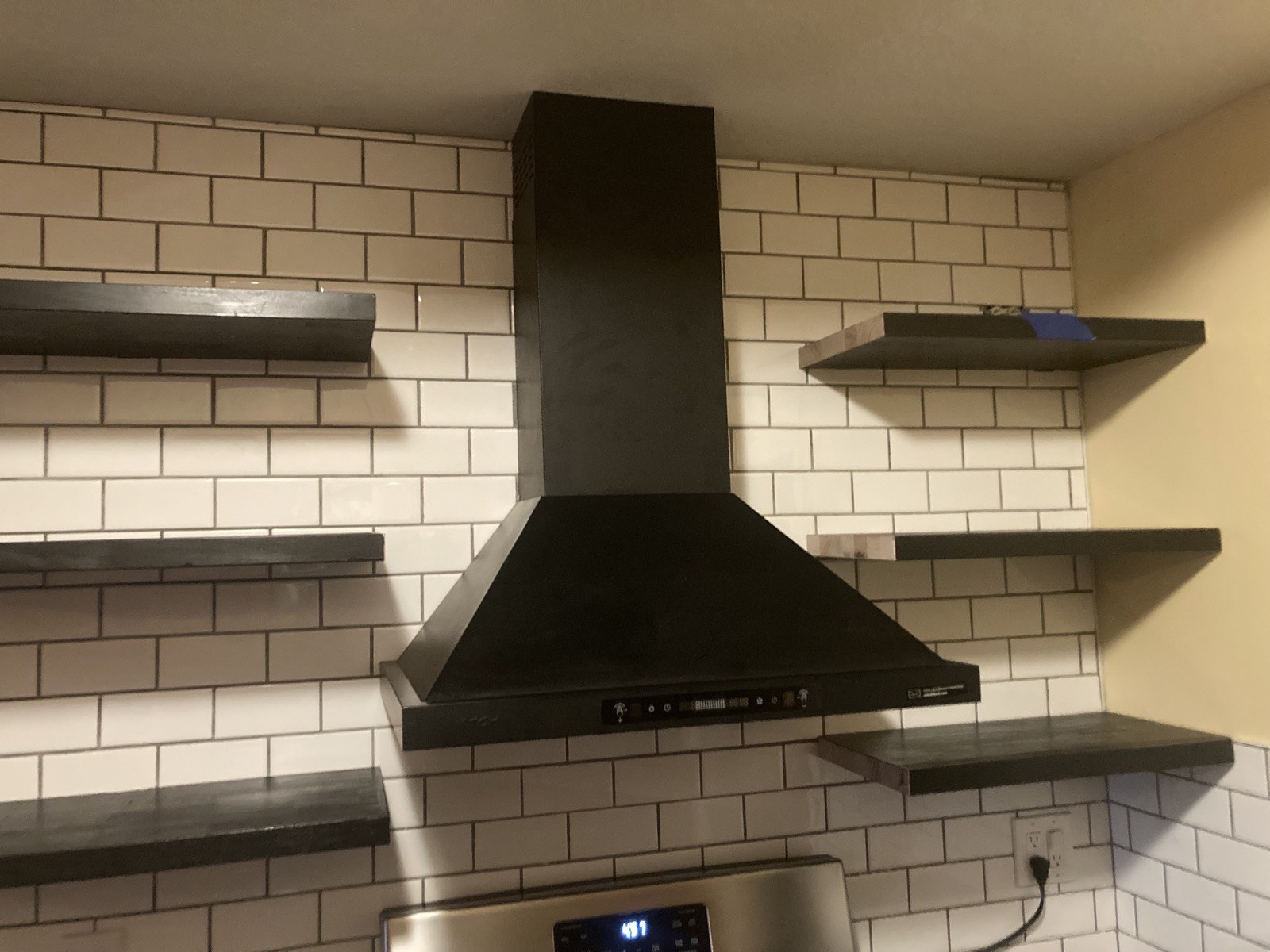 Close-up of the finished black range hood between floating wood shelves above the stove.