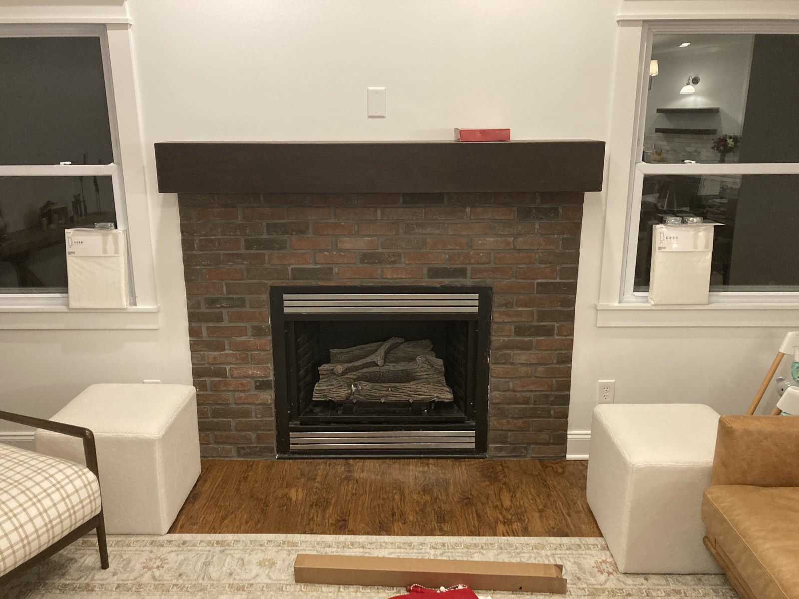 Brick fireplace with dark wood mantel flanked by two upholstered ottomans