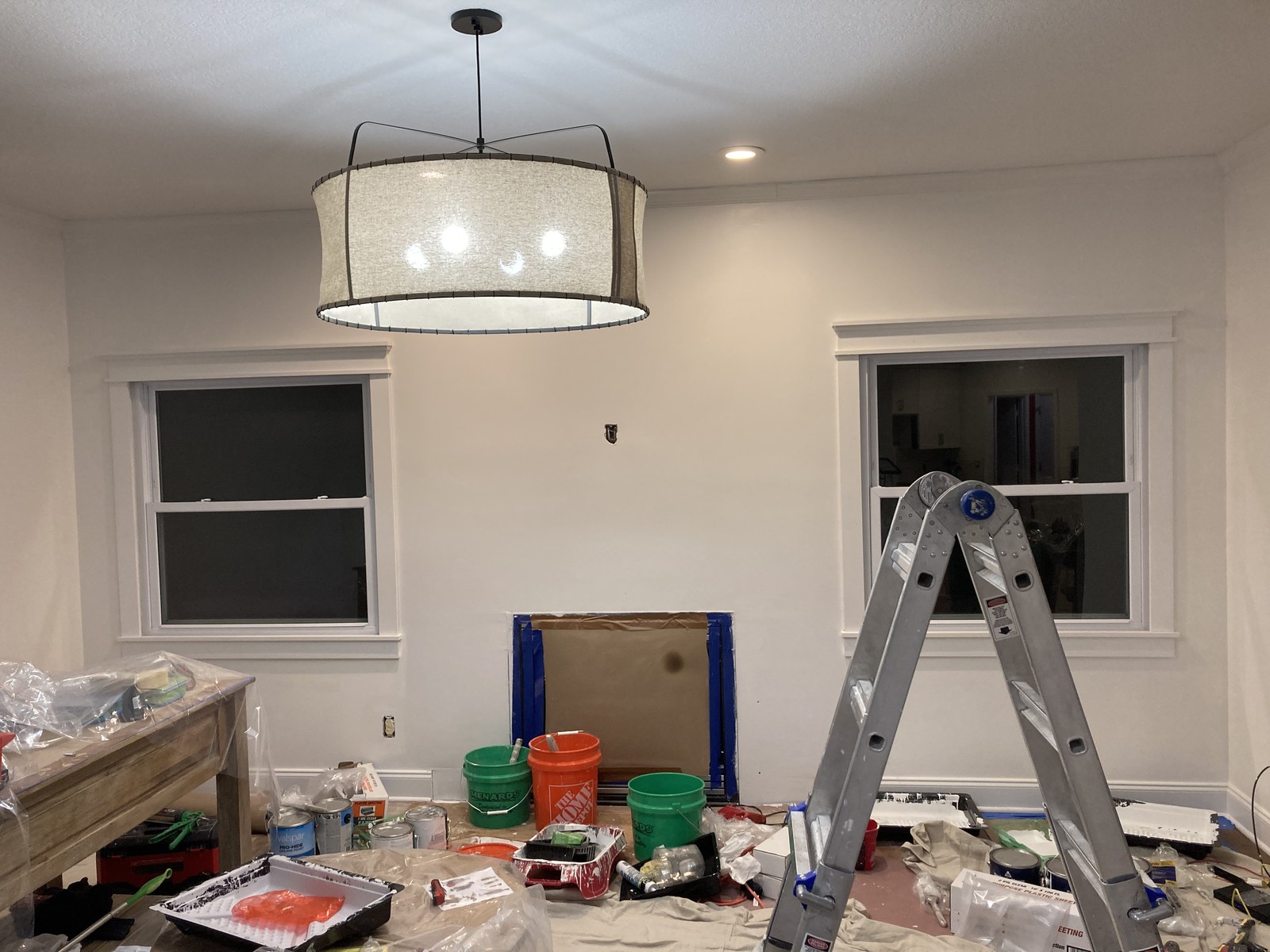 Ladder and paint buckets in a living room with a brick fireplace during painting