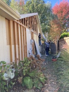 Gable wall stripped of all siding, bare studs and framing visible with two workers