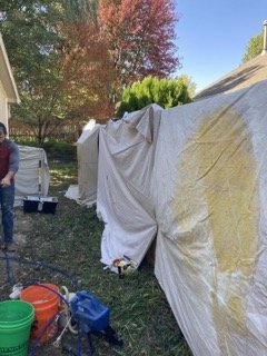 Tarps covering fence to mask it during paint spray, sprayer and buckets in foreground