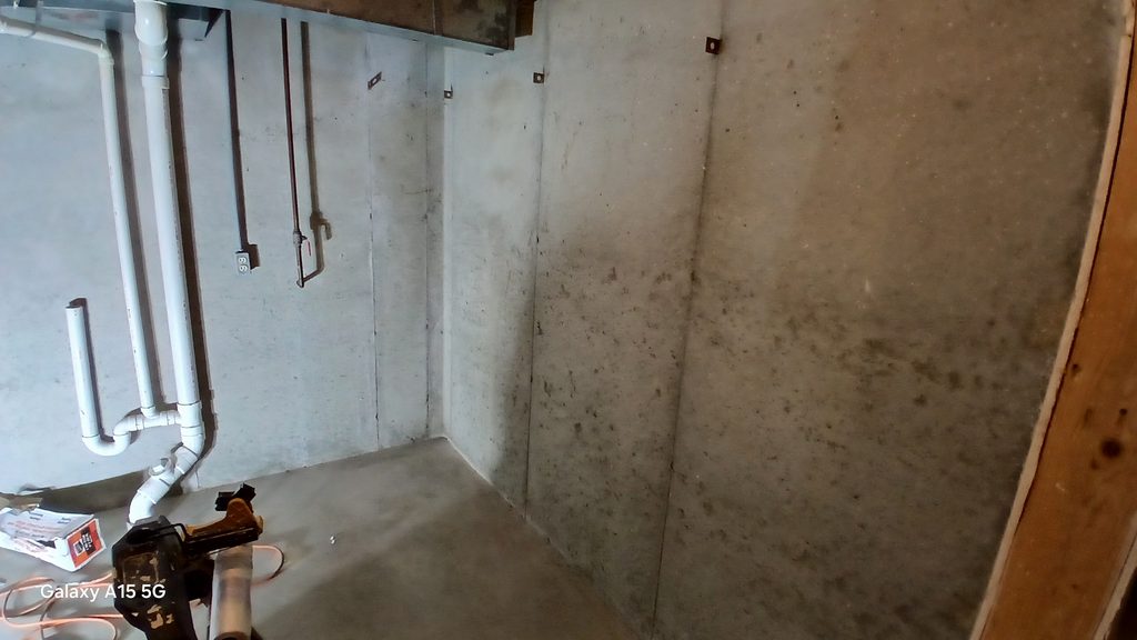 Bare concrete basement corner with exposed copper plumbing lines before framing.