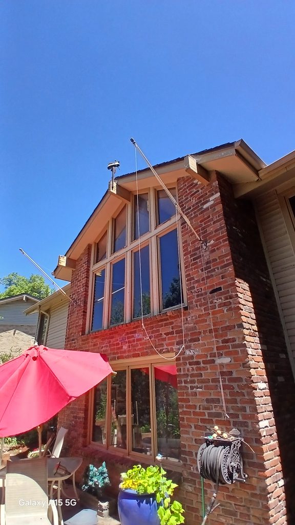 Exterior of a two-story brick house showing the tall window wall before window replacement, with rigging lines set up.