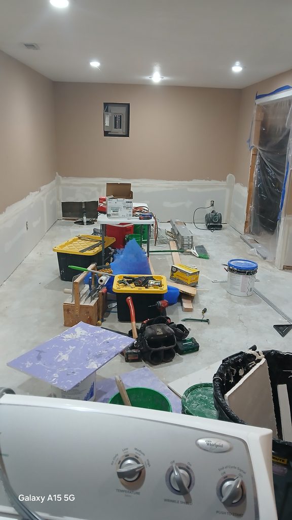 Basement living area with taped drywall, painted upper walls, and tools staged during the project.