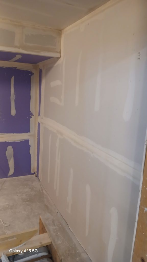 Taped and mudded purple drywall in the laundry room with a framed closet niche overhead.