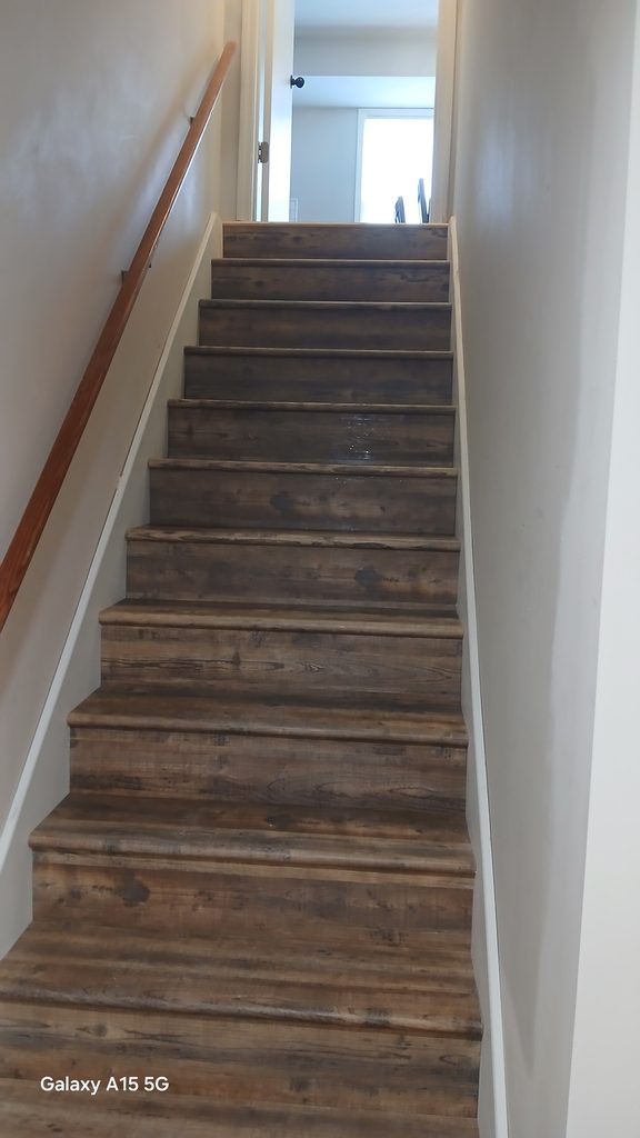 Finished basement staircase with vinyl plank treads and risers viewed from the bottom.