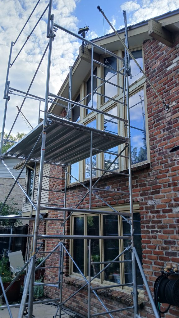 Scaffolding erected against a brick house to reach an 18-foot-high window wall.
