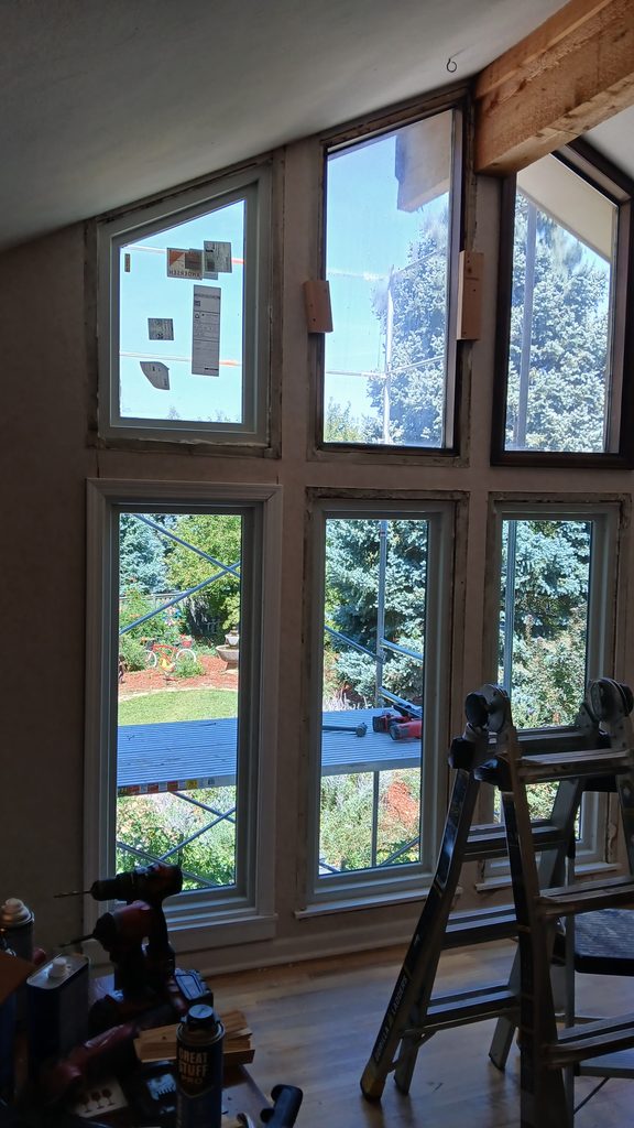 Mid-swap view of the window wall with new windows below and original windows with manufacturer labels still above.