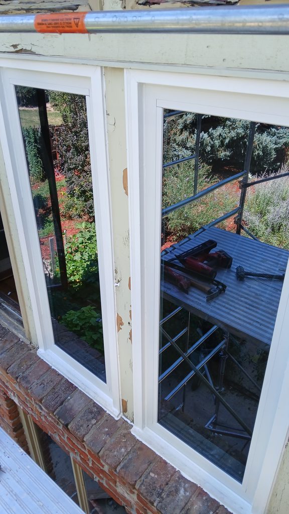 Exterior view of two newly installed windows with white trim, tools reflected in the glass.