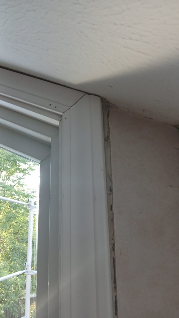 Close view of a white window casing corner joint next to unfinished drywall.