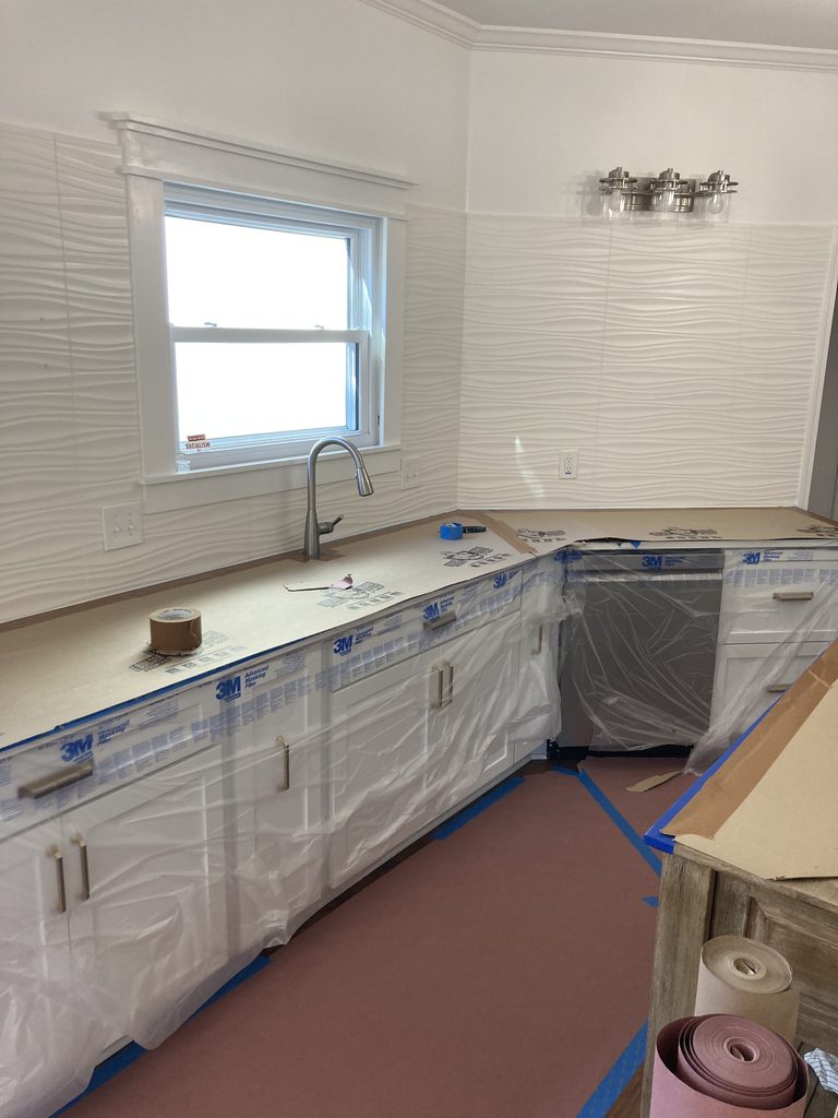 Wavy tile backsplash and cabinets covered in plastic before the kitchen remodel