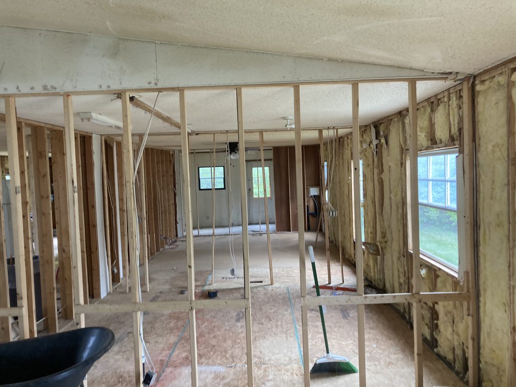 Exposed wall studs and pink insulation in a gutted single-wide living area.