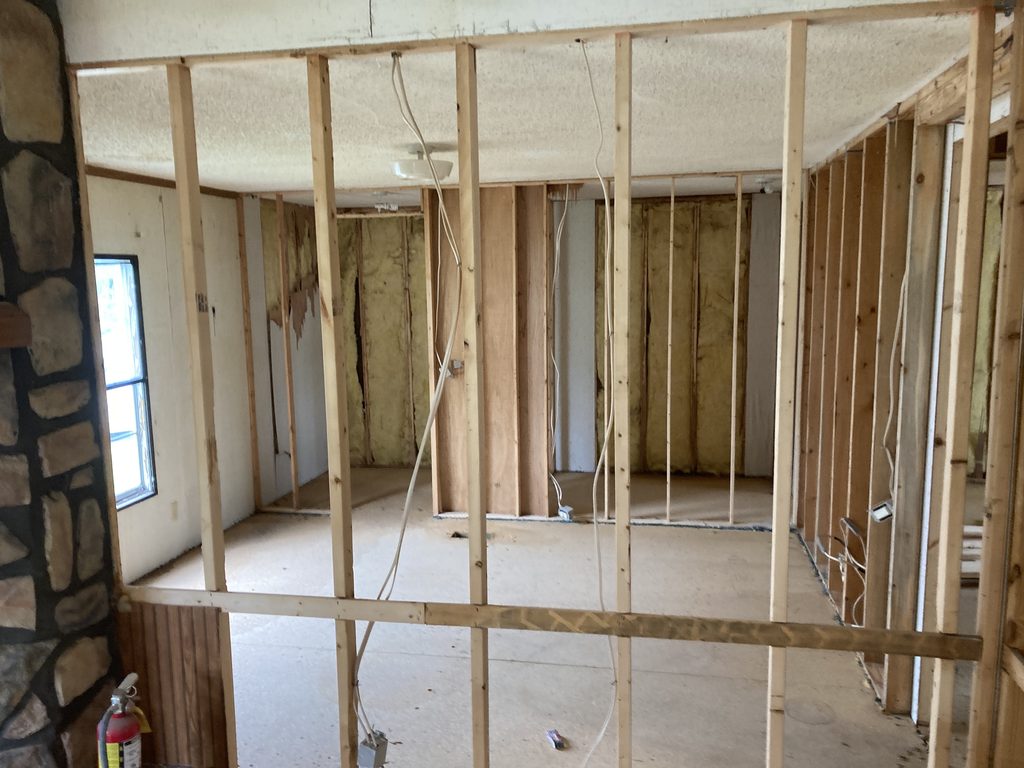 Wood stud framing and insulation beside a stone-clad fireplace column.