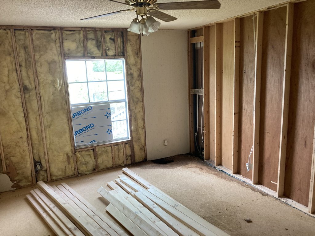 Insulated wall framing in a bedroom with framing lumber stacked on the subfloor.