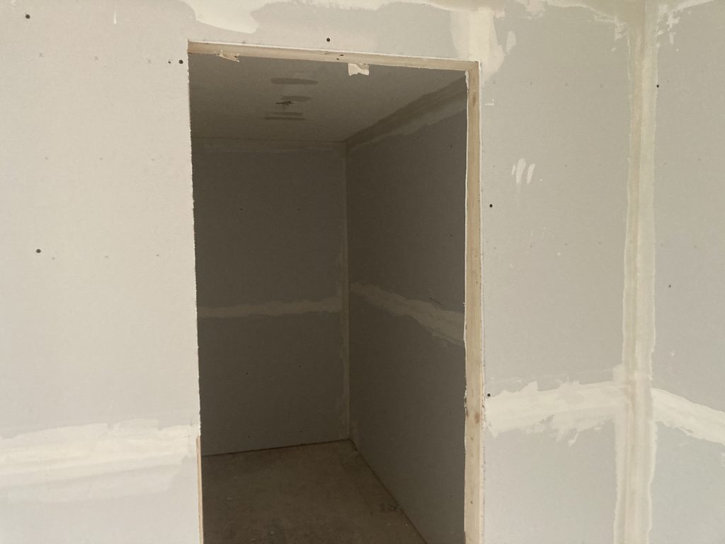 Taped and mudded drywall inside a small closet with the door open.