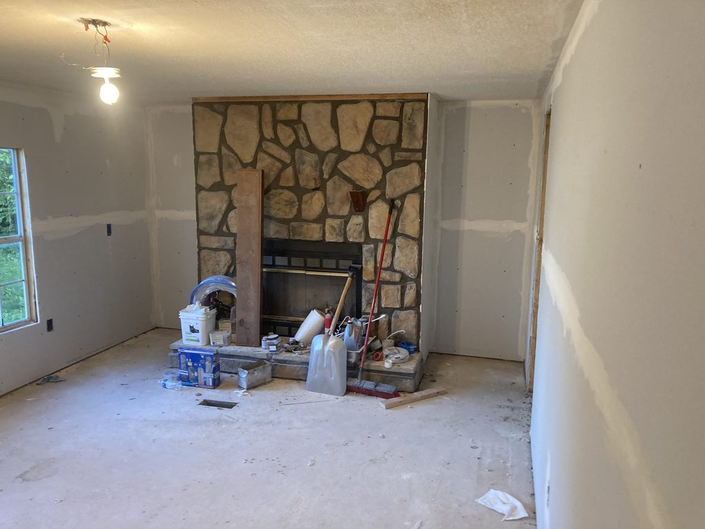 Stone fireplace surrounded by finished drywall with tools and buckets staged at the hearth.