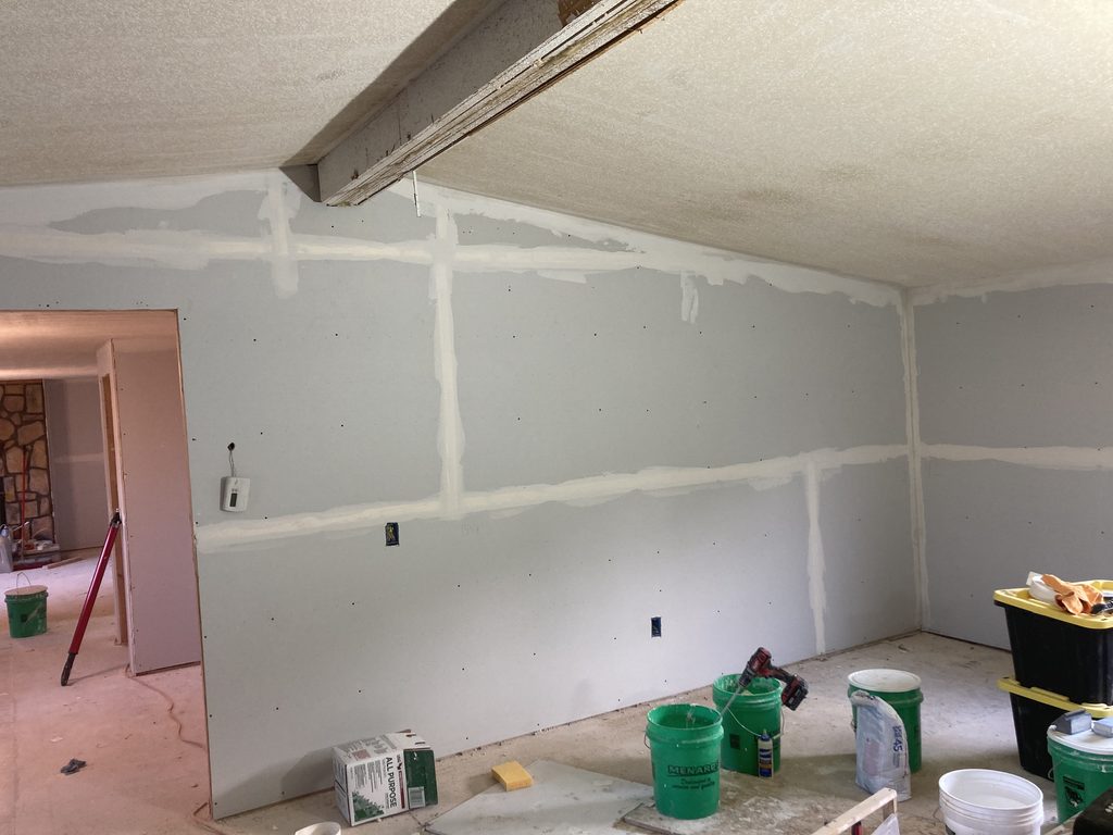 Finished drywall in a room with an exposed ceiling beam and hallway opening.