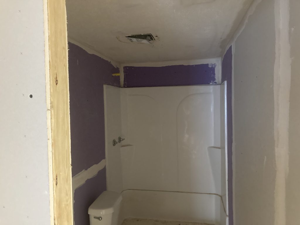 Small bathroom with a white tub and shower surround installed and walls primed purple.