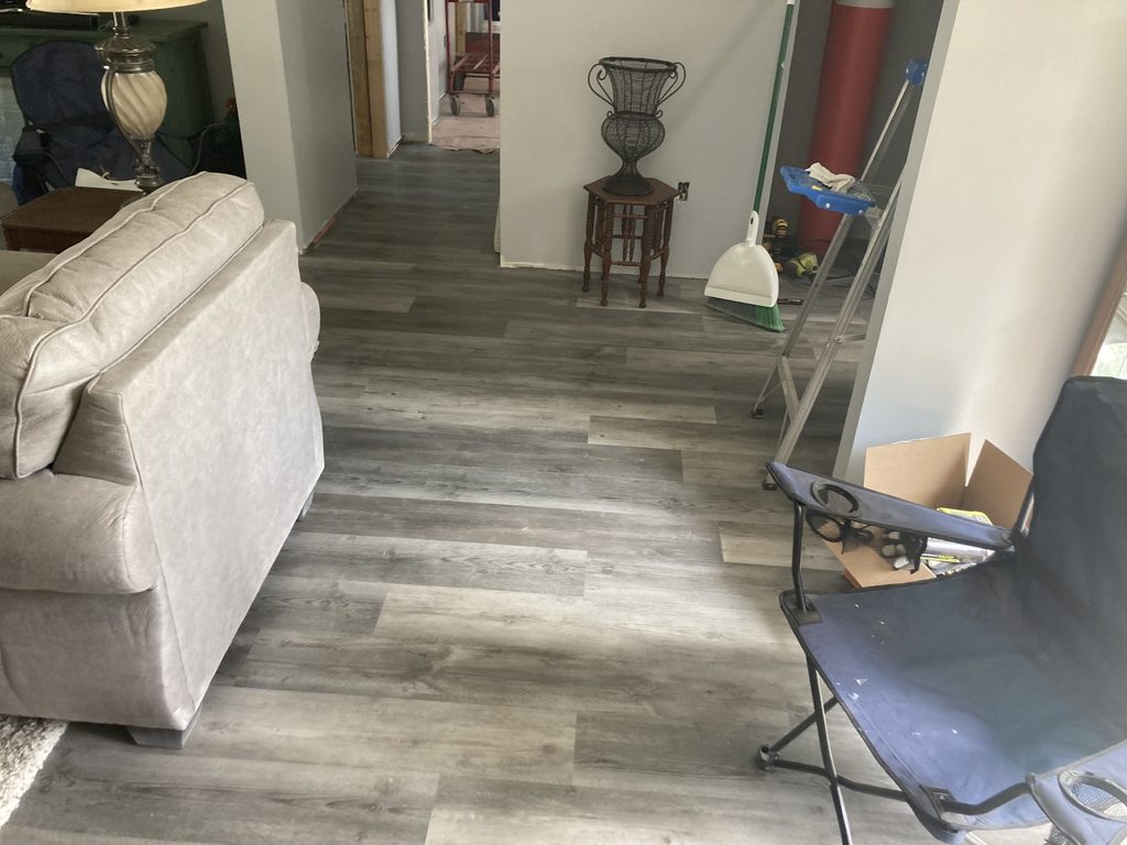 Finished gray vinyl plank flooring in a living room with a sofa and side table.