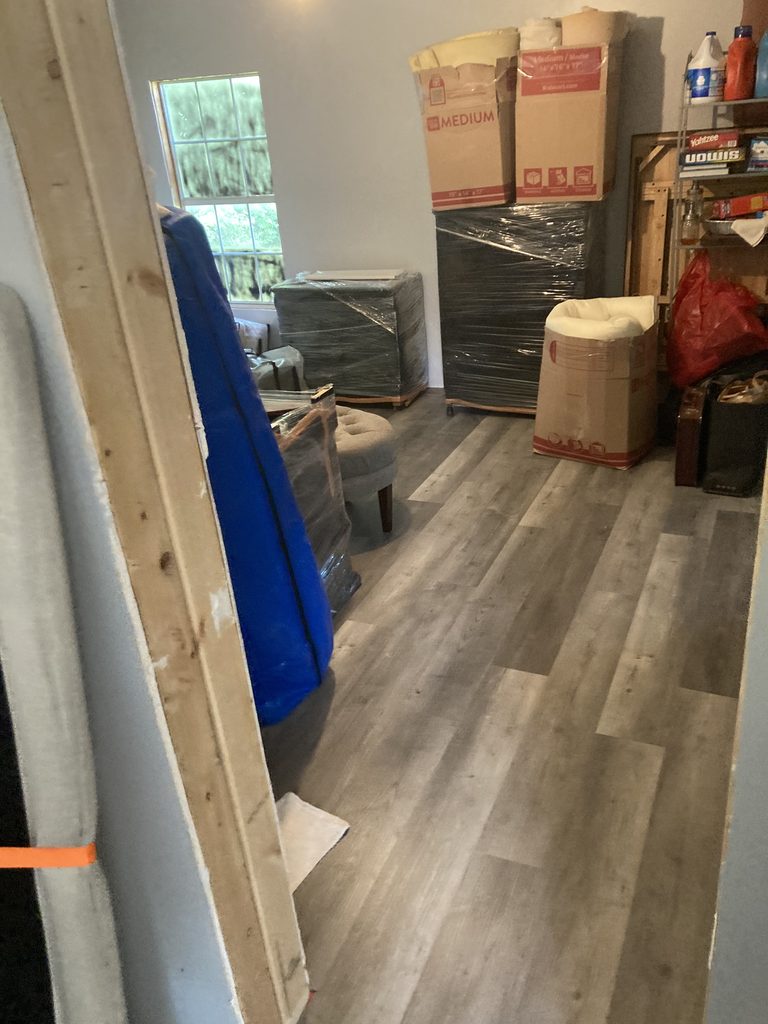 Moving boxes and wrapped furniture staged on finished vinyl plank flooring.