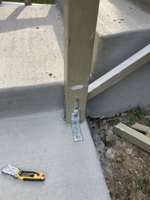 Close-up of a galvanized bracket securing a railing post to concrete steps.