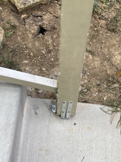 Close-up of a railing post base bolted down near a drilled anchor point in the yard.