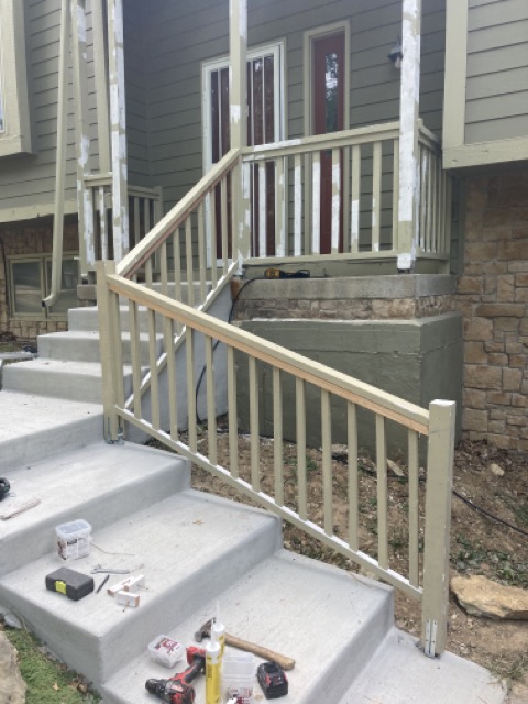 New wood handrail running down the concrete steps to the front porch.