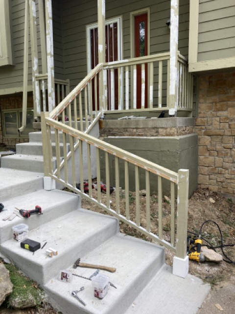 New railing with vertical spindles installed along the concrete steps by the front door.