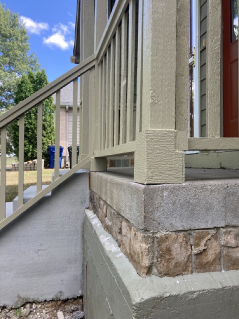 Finished porch railing and post detail beside the stone porch base and red front door.