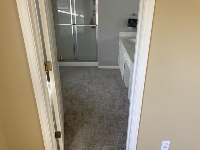 Doorway view of a carpeted bathroom with a glass shower door before the renovation.