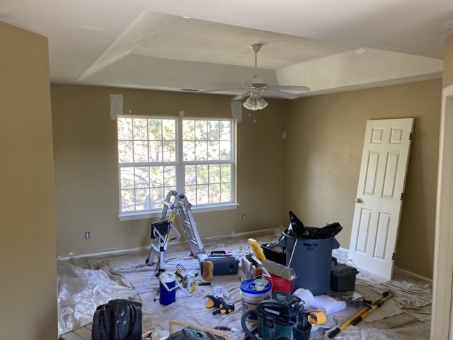 Bedroom tray ceiling and window with paint tools and drop cloths on the floor.