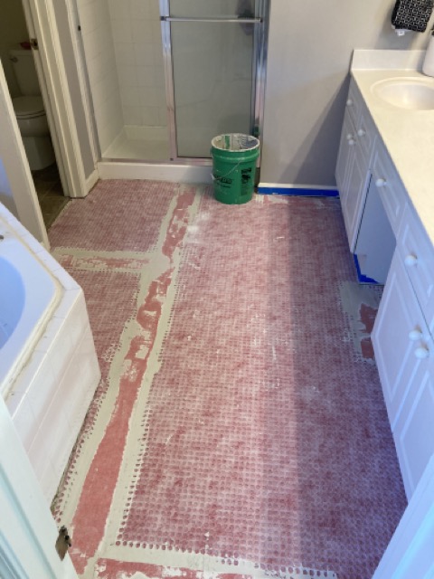 Bathroom floor prep with underlayment paper and a bucket near the vanity.