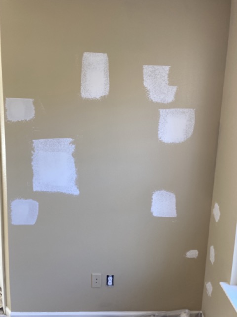 Wall with several drywall patches primed white before painting.
