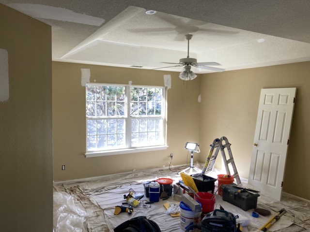 Bedroom tray ceiling and window with paint equipment set up on the floor.