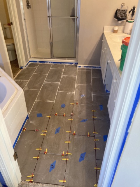 Gray tile floor freshly laid in the bathroom with spacers still in place.