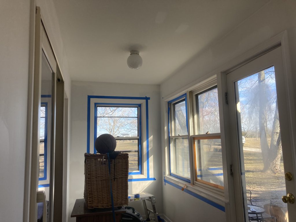 Sunroom with windows taped in blue painters tape and drop cloths down before painting.