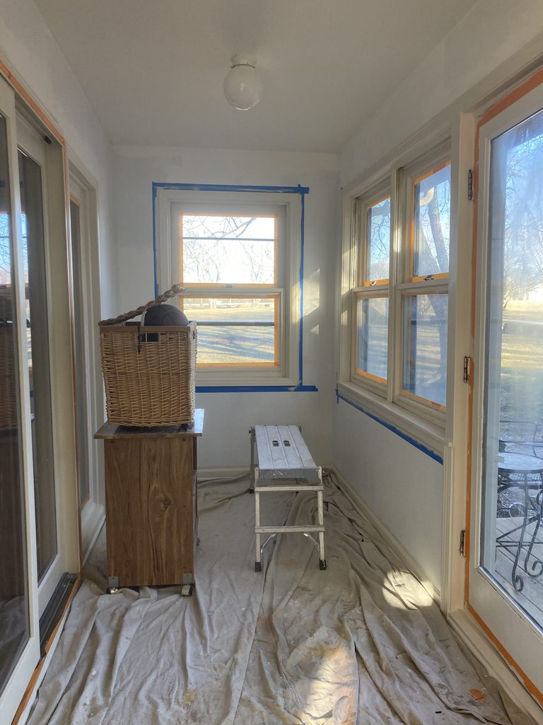 Sunroom hallway with taped windows, drop cloths, and a basket on a stand during the work.