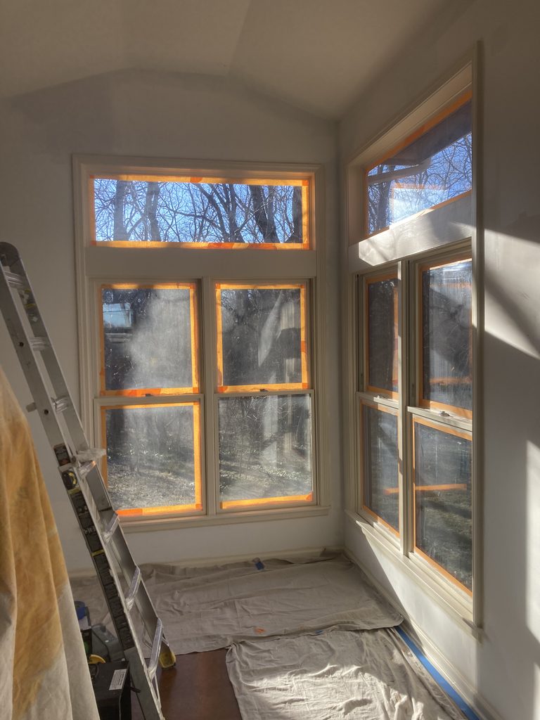 Bay window taped off with a ladder in front during paint preparation.