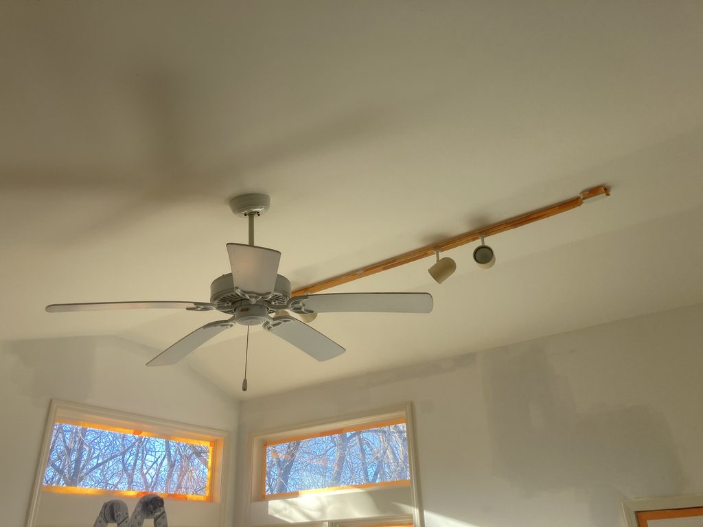 Ceiling fan and track lighting fixture with painter's tape marks along the ceiling seam.