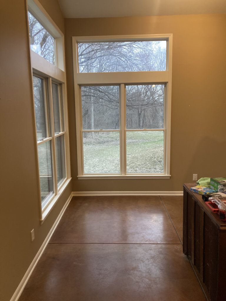 Finished sunroom with white-trimmed windows and repainted walls overlooking the yard.